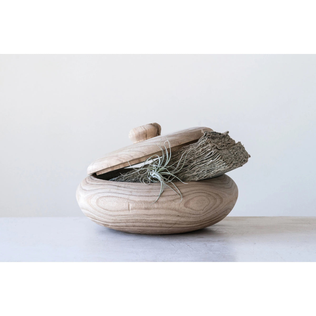 The PAULOWNIA WOOD CONTAINER by CREATIVE COOP is a round wood container with a matching lid, slightly open. The bowl and lid feature a smooth, light-colored finish that beautifully showcases the natural wood grain patterns. A small knob on top of the lid ensures easy lifting.
