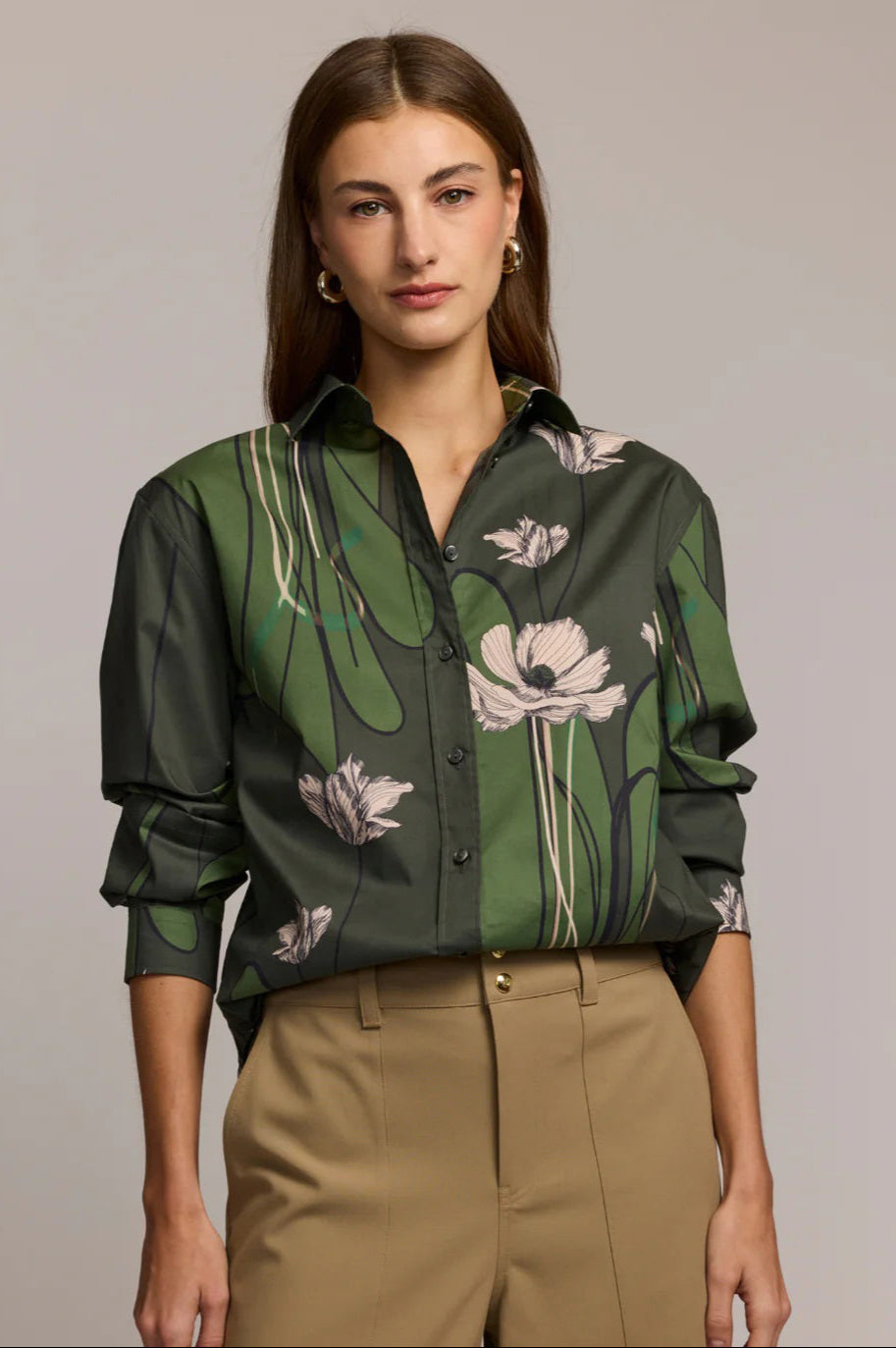 A woman with long brown hair wears the HINSON WU Halsey Long Sleeve Shirt in Poppy Print and tan pants, standing with her hands in her pockets against a neutral background.