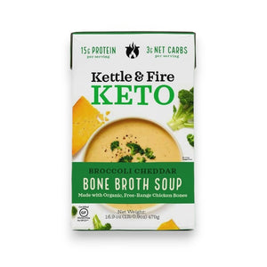 A 16.9-ounce (477g) carton of KETTLE & FIRE - BROCCOLI CHEDDAR KETO SOUP, featuring organic broccoli and sharp cheddar. The front label highlights 15g of protein per serving, 3g net carbs, and chicken bone broth made from organic, free-range chicken bones. The package is white with green accents.