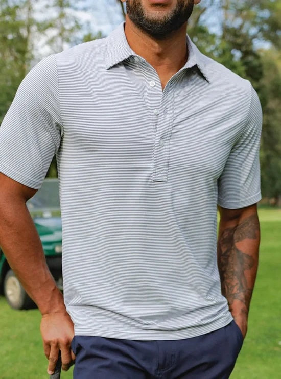 A smiling man with short hair and a beard wears the CRIQUET - Performance Sport Range Polo in Hobby Stripe - Gray as he holds a canned drink in a green koozie, facing slightly to the left against a plain white background.
