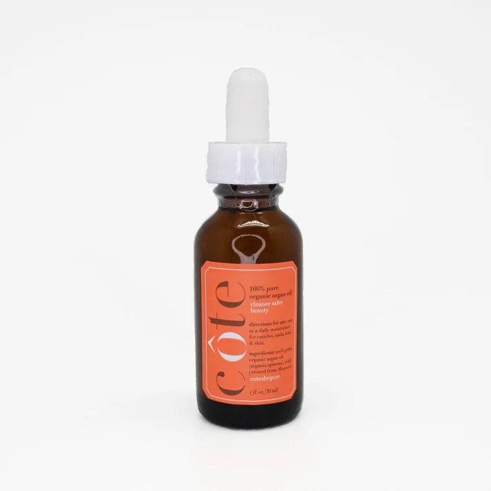 A small amber dropper bottle with a white lid is labeled "COTE" in orange text. It contains COTE - ORGANIC ARGAN OIL, 100% pure and ideal as a nourishing moisturizer. The bottle is placed on a plain white background.