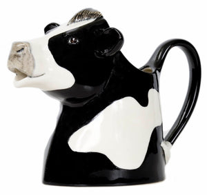 The QUAIL DESIGNS QUAIL CERAMICS - FRESIAN COW JUG MEDIUM is a handpainted stoneware jug shaped like a black and white cartoon cow, with the handle as the tail and an opening in the head. Charming and dishwasher safe.