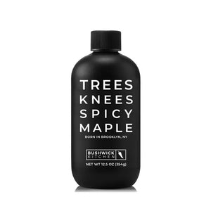 A black bottle with minimalistic design and white text that reads "TREES KNEES SPICY MAPLE, BORN IN BROOKLYN, NY." Below the text is the "BUSHWICK KITCHEN" logo, along with "NET WT 12.5 OZ (354g)." The bottle features a screw cap. This BUSHWICK KITCHEN - 'TREES KNEES' Spicy Maple Syrup is infused with habanero for the perfect kick.