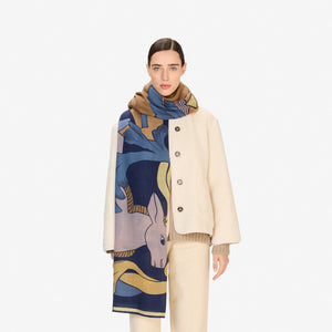 The INOUI CAVALE HORSE WOOL SCARF in navy features an abstract design with stylized tan and lavender rabbits among blue and yellow leafy shapes, all set against a dark blue background.