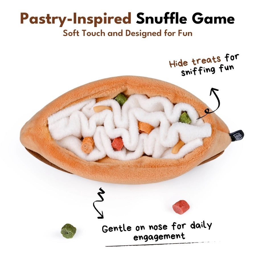 Introducing the CHOCOLATE ÉCLAIR SNUFFLE &amp; CRINKLE DOG TOY by CHEWFFON—a plush dog toy shaped like a chocolate éclair with tan and brown fabric, topped with white squiggly lines resembling icing. This interactive dog toy features snuffle and crinkle elements for extra fun during playtime, making it perfect for pups who love cuddle-worthy companions.