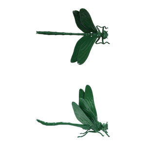 A pop-up book on a wooden surface showcases two large green CAST IRON DRAGONFLY sculptures by CREATIVE COOP, emerging from its pages against a plain light background.