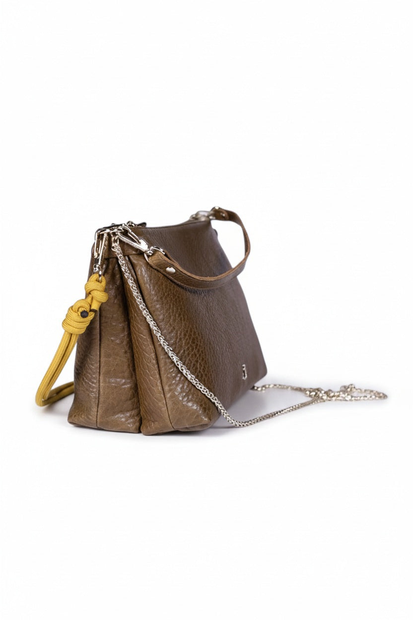 The CRAIE STUDIO DUO BUBBLE UMBER HANDBAG features brown textured vegetable tanned leather with a shoulder strap, silver chain detail, a small front logo, and yellow knot accents on the sides, displayed against a white background.