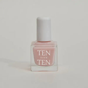 A glass bottle of TENOVERTEN - NAIL POLISH from the brand TEN OVER TEN, featuring a white cap and a dusty pink nail color. The front label displays "TEN OVER TEN" in white uppercase letters. This vegan, eight-free formula ensures both beauty and peace of mind. The background is plain and light-colored.