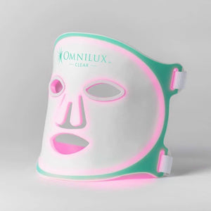 The OMNILUX CLEAR MASK, offering white and teal LED light therapy for acne with eye, nose, and mouth cutouts, uses blue and red clinically proven light therapy. It includes a controller, charging accessories, and an instruction manual.