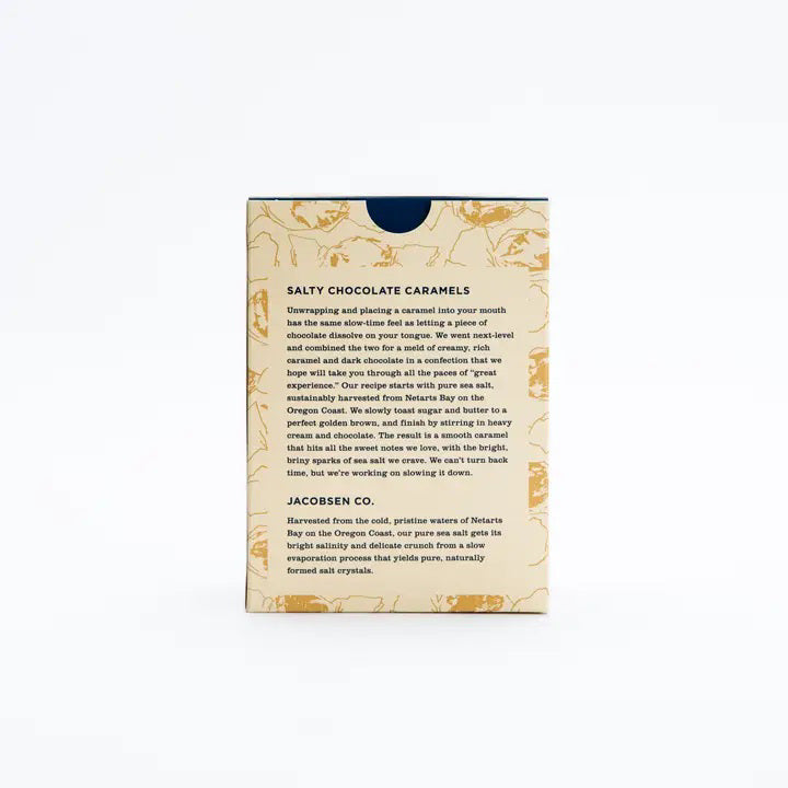A rectangular box of JACOBSEN SALT CO. CHOCOLATE CARAMELS WITH SEA SALT stands on a light surface, featuring tan packaging with brown abstract patterns and a white label displaying the product name in black and gold.
