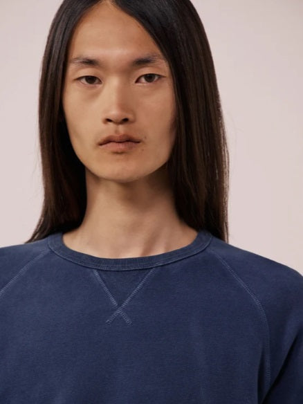A person with long, straight hair is wearing the HARTFORD - LIGHT FLEECE SWEATSHIRT IN NAVY by HARTFORD and light-colored pants, standing with one hand in their pocket against a plain white background.