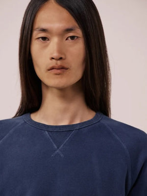 A person with long, straight hair is wearing the HARTFORD - LIGHT FLEECE SWEATSHIRT IN NAVY by HARTFORD and light-colored pants, standing with one hand in their pocket against a plain white background.