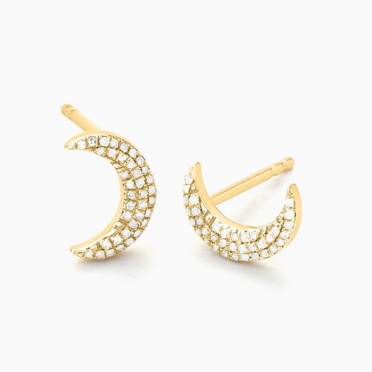 A close-up of a woman’s ear wearing the ELLA STEIN - MINI MOON STUD EARRINGS by ELLA STEIN, featuring small crescent moon shapes adorned with sparkling natural diamonds set in gold-plated stainless steel. Brown hair with blonde highlights is visible in the background.