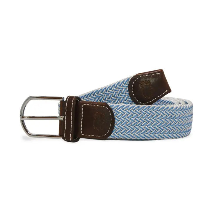 The ROOSTAS - SARASOTA WOVEN STRETCH BELT by ROOSTAS features sky blue and white weaving, brown leather ends, and a silver buckle, shown coiled with the buckle at the front.