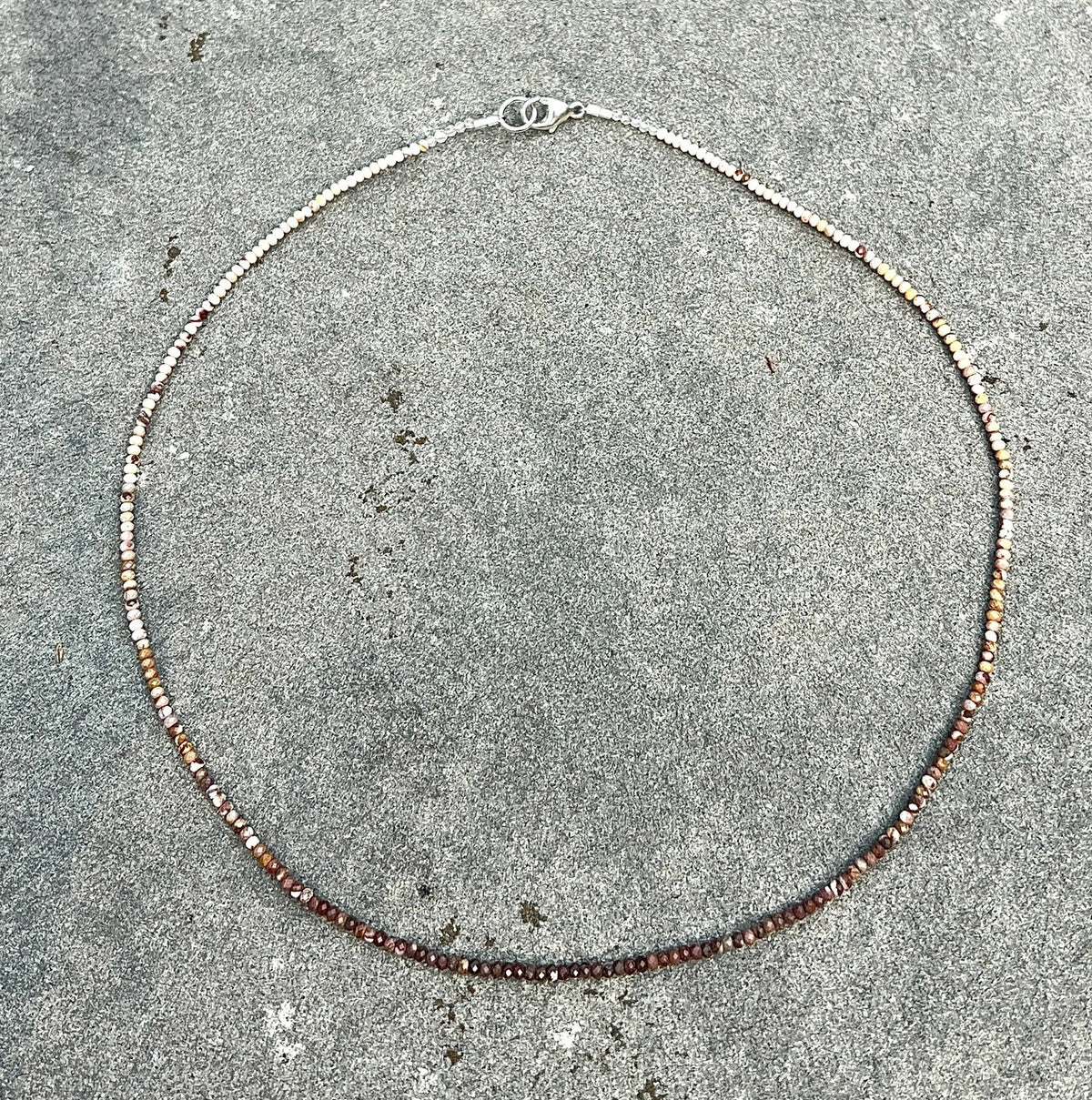 The ANN LIGHTFOOT - Mookite Ombre Ras du Cou Necklace features small, round brown and pink beads with a sterling silver clasp, shown in a circular shape on a white background.