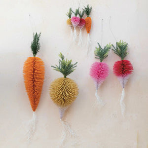 The CREATIVE COOP FLOCKED BOTTLE BRUSH VEGETABLE ornaments, featuring green tops and white roots in assorted carrot and radish styles, hang decoratively on a light beige wall.