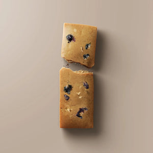 A purple STARS+HONEY - PEANUT BUTTER BLACKBERRY protein bar rests on a beige surface, with its wrapper highlighting 10g collagen, 15g protein, and 2g sugar.