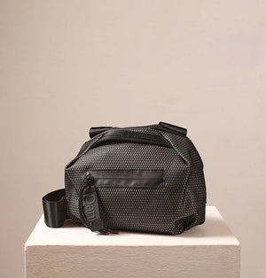 A person in a light beige suit carries the DANIELLA LEHAVI - BONNIE TRAVEL CROSSBODY, a large brown vegan bag with black zipper and strap, shown from shoulders to mid-thigh against a plain background.