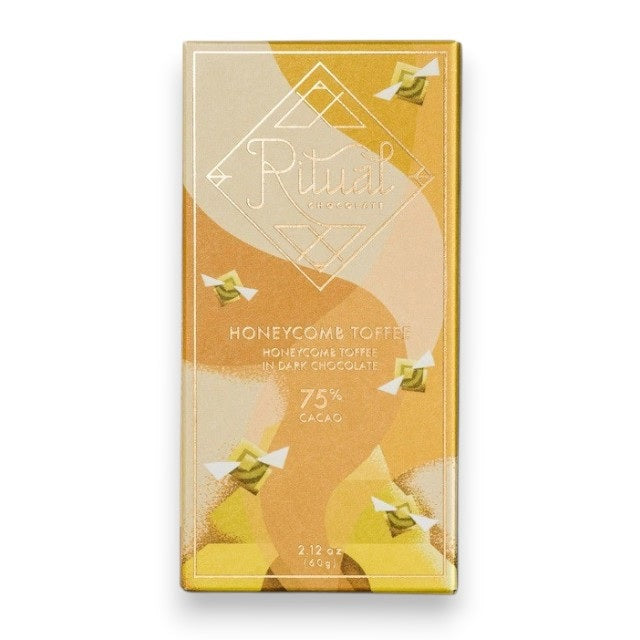 A gold and yellow RITUAL CHOCOLATE - HONEYCOMB TOFFEE CHOCOLATE BAR wrapper with geometric designs holds a 2.12 oz (60 g), 75% cacao single origin dark chocolate bar, displayed on a marble background.