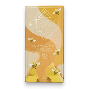 A gold and yellow RITUAL CHOCOLATE - HONEYCOMB TOFFEE CHOCOLATE BAR wrapper with geometric designs holds a 2.12 oz (60 g), 75% cacao single origin dark chocolate bar, displayed on a marble background.