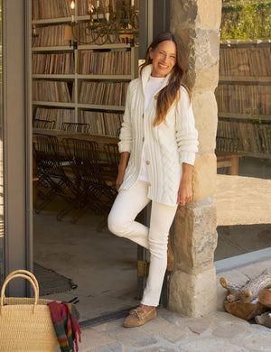 The FRANK & EILEEN Cotswolds Cable Knit Cardigan in ivory is a chunky Italian cotton sweater, featuring a ribbed shawl collar, braided cable knit pattern, and brown buttons.