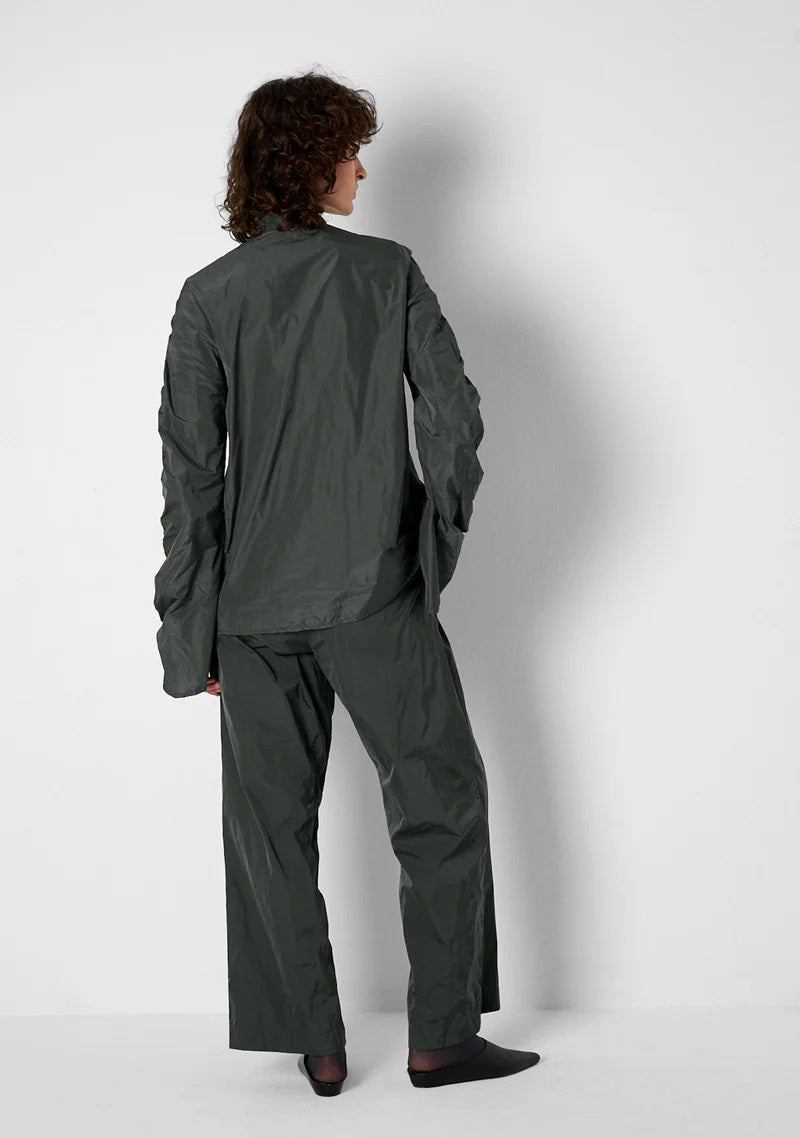 A close-up of KATHARINA HOVMAN&#39;s Easy Pants in anthracite taffeta reveals a textured, possibly dark fabric with a crumpled surface and hints at an elastic waistband due to lighting variations.