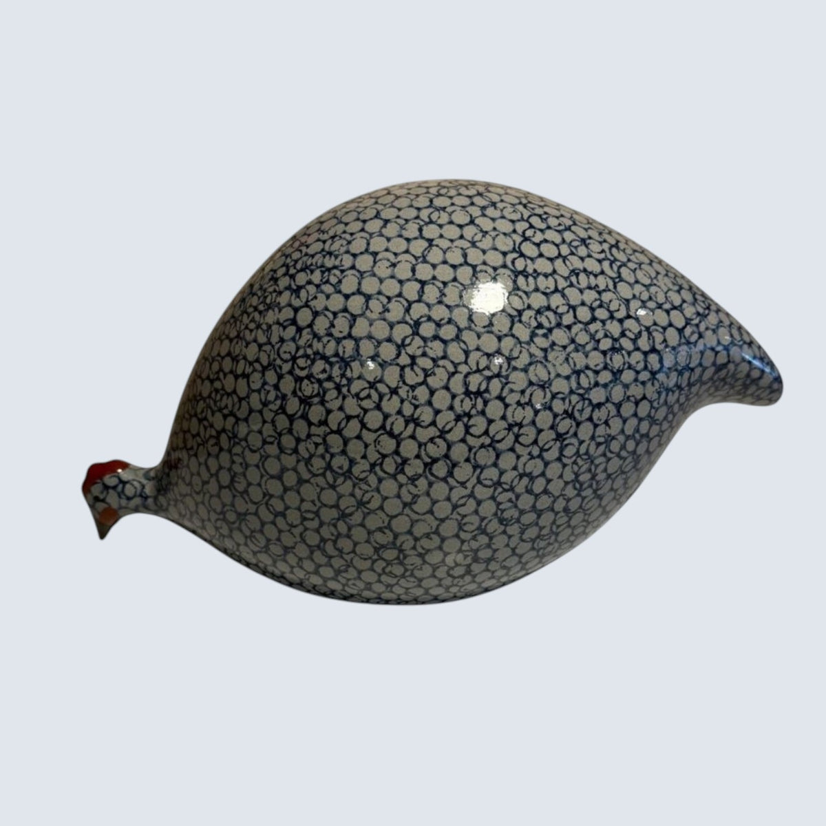 The LES CERAMIQUES DE LUSSAN - LARGE PECKING CERAMIC FRENCH GUINEA IN BLUE SPOTTED COBALT sculpture showcases a pattern of small blue circles on a white background. It is elegantly displayed on a simple, light-colored pedestal against a neutral backdrop, reflecting the artistry of traditional ceramic workshops.