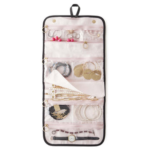 The KUSSHI - LARGE TRAVEL JEWELRY ORGANIZER by KUSSHI is a rolled-out jewelry organizer made with a premium nylon exterior. It features multiple transparent zippered compartments, offering compact travel storage for rings, earrings, bracelets, necklaces, and a watch. The organizer comes in pink with black edges and includes a black hanging loop at the top.