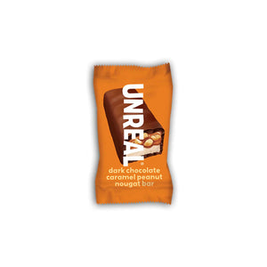 An orange-wrapped UNREAL - DARK CHOC CARAMEL PEANUT NOUGAT BAR with a bite revealing layers of caramel, peanuts, and nougat inside. Crafted with non-GMO ingredients, this healthier candy bar alternative features the product name and flavor in white text on the wrapper under the UNREAL brand.
