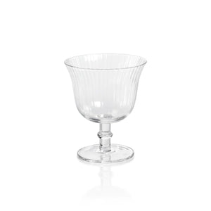 The JULIEN OPTIC COCKTAIL GLASS by ZODAX is a transparent glass goblet with a fluted pattern, featuring a wide bowl, a short stem, and a round base. With a capacity of 240 ml, the glass is empty and sits on a plain white background, creating reflections on the surface below.
