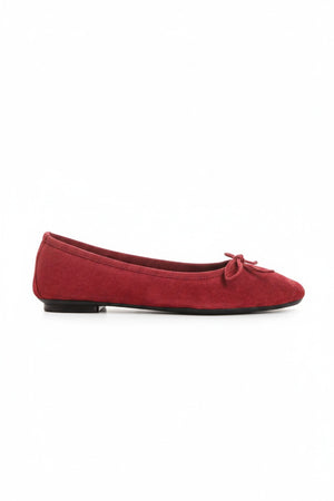 A person wearing blue jeans and REQINS - HARMONY Suede Ballerina Flats in cerise stands on a light-colored floor.