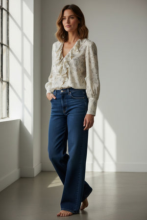 The RUFFLED BLOUSE by MOMONI is a cream-colored, long-sleeved bohemian top made in Italy, adorned with ruffle details at the neckline and a delicate black line print featuring stars and animals. Crafted from luxurious silk crêpe de chine, it offers an effortlessly elegant look.