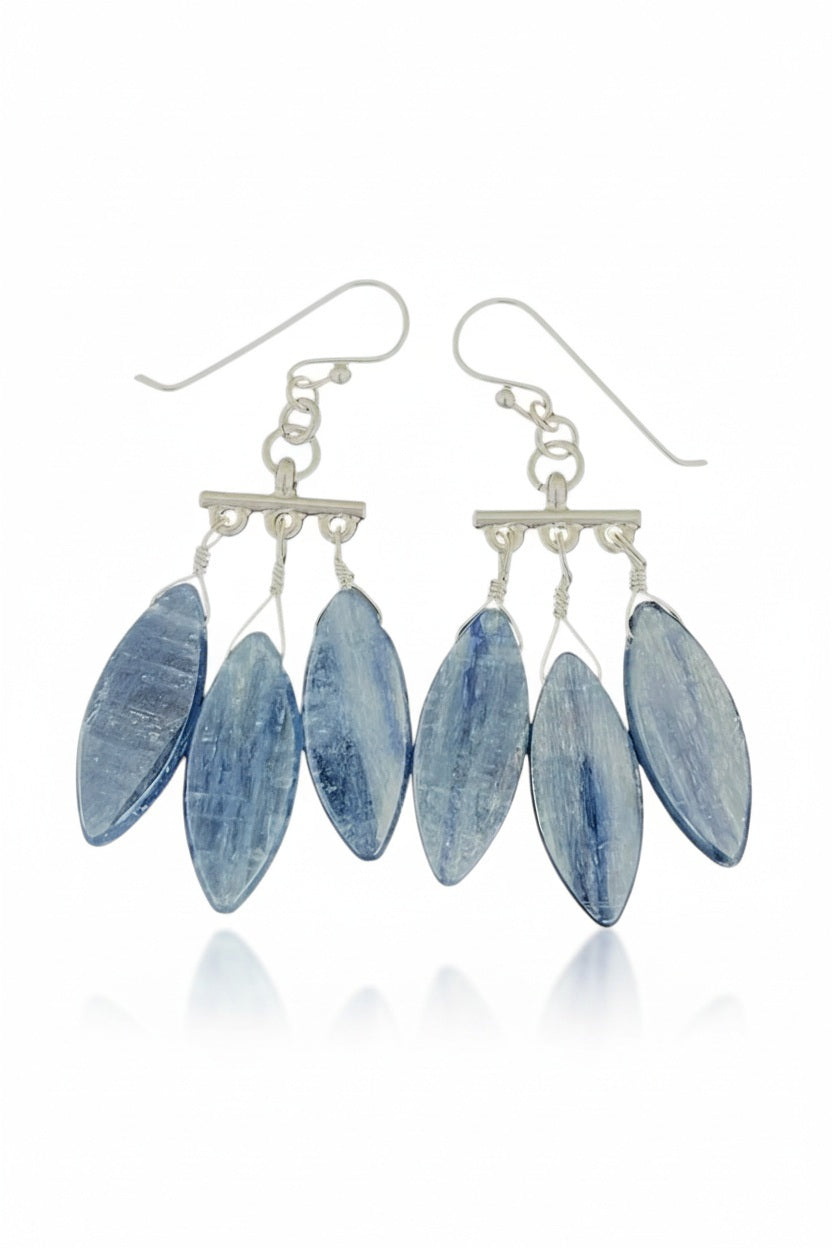 The ANN LIGHTFOOT Kyanite Chandelier Triple Drop Earrings by ANN LIGHTFOOT showcase three elongated blue kyanite pendants delicately suspended from each sterling silver earring, elegantly presented against a white background.