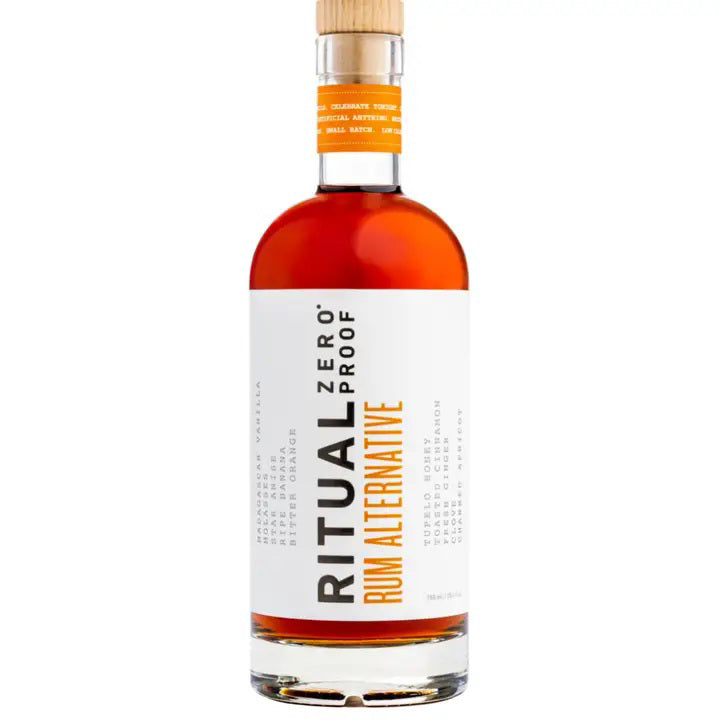 A bottle of RITUAL ZERO PROOF- RUM ALTERNATIVE by RITUAL ZERO PROOF, featuring a tan cap, amber liquid, and a white label with bold black and orange text describing this non-alcoholic rum alternative.