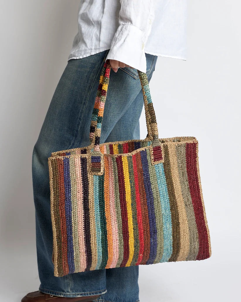 The GABRIELE FRANTZEN LITTLE SISTER WEEKENDER BAG CIRCUS is a large rectangular raffia bag with colorful vertical stripes, two matching handles, and a flat base—perfect as a stylish weekender.