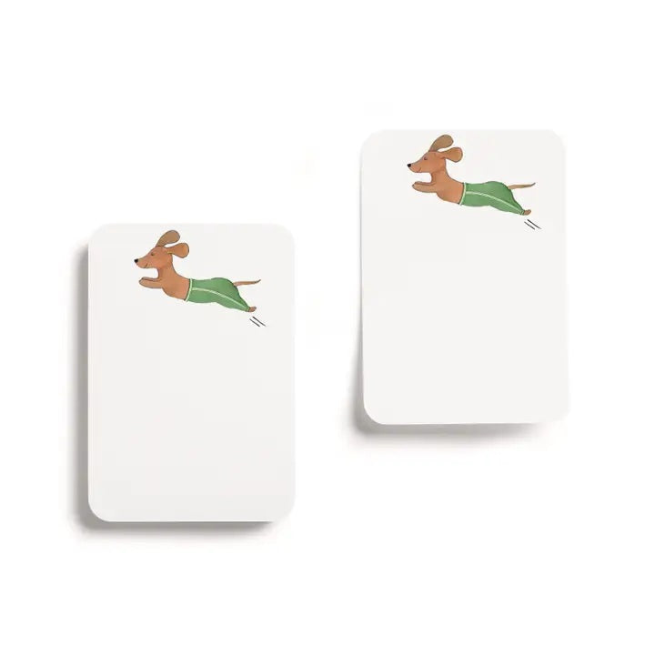 E. FRANCES PAPER's "Little Stickies Off Leash" notepad features a brown dachshund in green pants, with a backing card decorated with playful cartoon dogs on a green background—perfect dog stationery for any pup lover.
