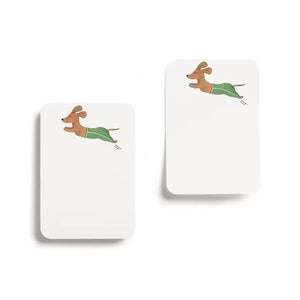 E. FRANCES PAPER's "Little Stickies Off Leash" notepad features a brown dachshund in green pants, with a backing card decorated with playful cartoon dogs on a green background—perfect dog stationery for any pup lover.