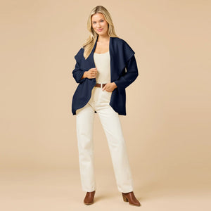 A woman wears an off-white SOFTIES - DREAMTECH EXAGGERATED COLLAR CARDIGAN with an exaggerated waterfall collar, cinched at the waist with a thin belt, and holds a matching handbag.