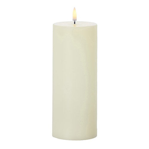 Introducing the Ivory Pillar Candle 3x9" by RAZ Imports, a sophisticated battery-operated candle designed with a tall, cylindrical shape and crafted from white wax, complete with a small yellow flame for elegant ambiance.
