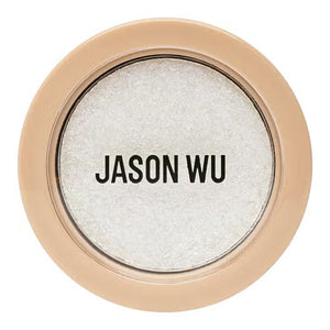 A circular makeup compact named "READY TO SHIMMER HEAVENLY 2" by JASON WU BEAUTY features a beige outer rim and a transparent lid, revealing a shimmery white powder inside. The bold black text "JASON WU" is printed on the lid, making it ideal for applying with an eye shadow brush to enhance the shimmer effect on your eyelids.