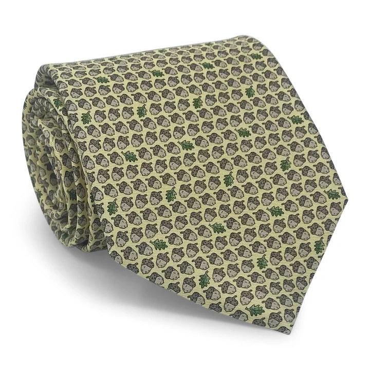 The PETER-BLAIR - ACORNS SILK TIE IN YELLOW by BIRD DOG BAY is a handmade yellow necktie from New York, adorned with a repeating pattern of brown acorns and occasional green oak leaves.