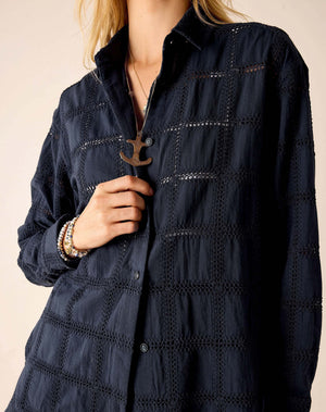 A woman with long blonde hair wears the MERSEA Brontë Button Up Shirt in Navy Crochet—a relaxed, textured long-sleeve shirt—paired with matching shorts, standing in profile against a light beige background.