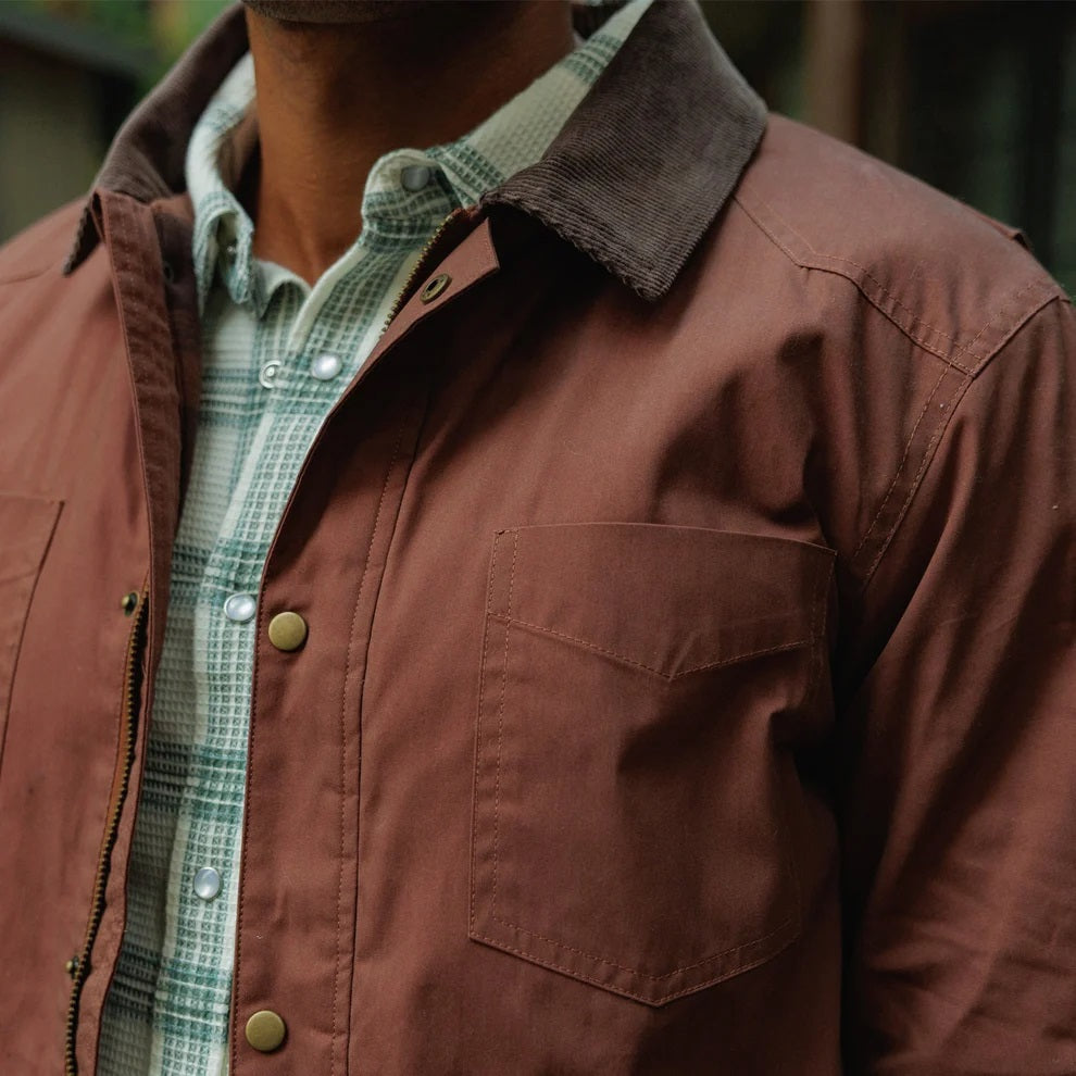Close-up of the interior of a brown plaid CRIQUET - WAXED RANCH JACKET IN BOURBON, showing a white “Clubhouse Collection” brand label with a blank line for a player’s name.
