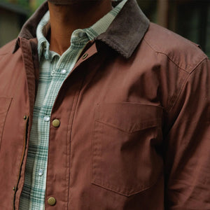 Close-up of the interior of a brown plaid CRIQUET - WAXED RANCH JACKET IN BOURBON, showing a white “Clubhouse Collection” brand label with a blank line for a player’s name.