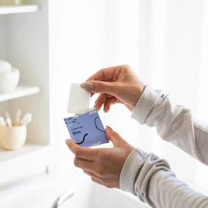 A CORNEA CARE packet, labeled "CORNEACARE - RISE EYELID WIPES," sits against a light blue backdrop with abstract wave and dot patterns. Infused with tea tree oil, it elegantly alleviates eye dryness.