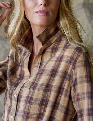 A woman stands in a sunlit room, smiling with curly hair, wearing the FRANK & EILEEN EILEEN Relaxed Button Up Shirt in Italian Flannel Gold Brown Plaid, paired with blue skinny jeans and brown ankle boots.