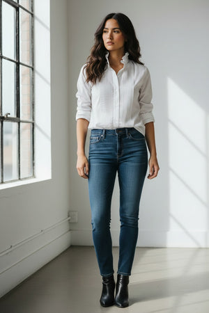 A blonde older woman wears the KMJ - SOUTHERN LOVER TUX blouse by KMJ and blue demi-boyfriend jeans with a turquoise necklace, looking down and tucking her hand in her waistband, set against a plain white background.