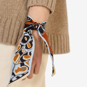 The INOUI EDITIONS - PAPILLON (BUTTERFLIES) SILK RIBBON by INOUI features a butterfly wing print in orange, black, white, and yellow—an elegant silk scarf to elevate any outfit. Displayed on a white background.