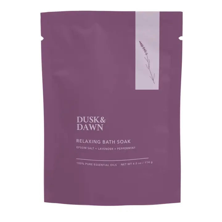 A purple pouch from GIFTEN MARKET, labeled "RELAXING BATH SOAK - LAVENDER AND PEPPERMINT POUCH," contains a soothing bath soak with Epsom salt, lavender, and peppermint essential oils. The minimalist packaging features a small illustration of a lavender sprig. Net weight: 4 oz. (114 g).