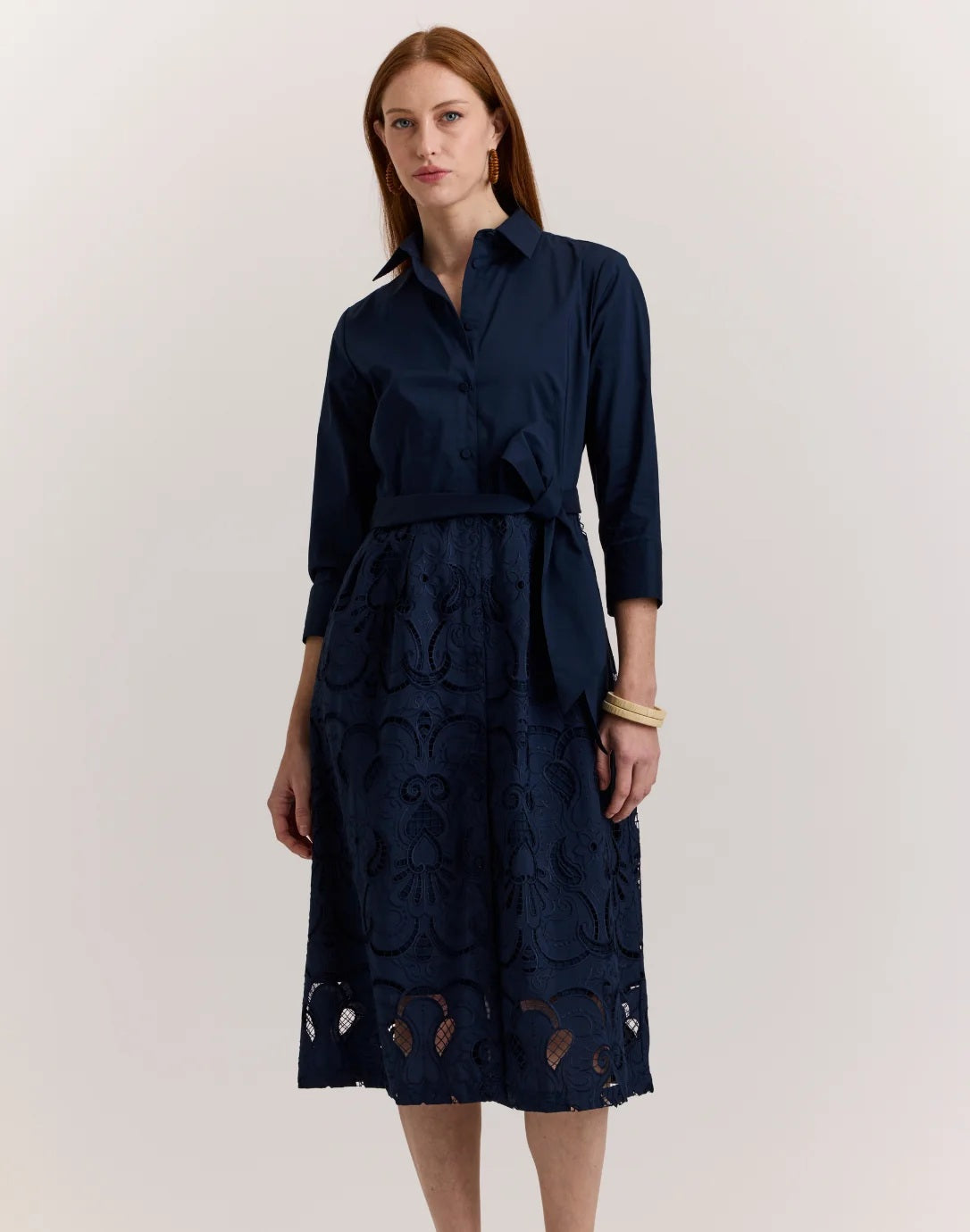 A woman stands against a plain light background wearing the HINSON WU Robin 3/4 Sleeve Eyelet Embroidery Dress in navy, featuring a collared neckline, belted waist, and an elegantly detailed lace-patterned skirt.